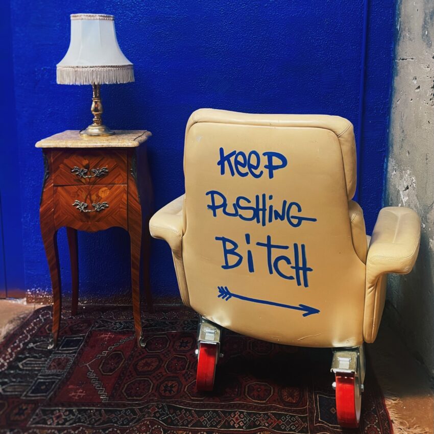 fauteuil en cuir sur roues vintage taggué "keep pushing bitch", monté sur roues rouges
